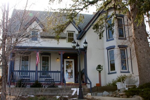 A charming two-story house with a porch, American flag, and decorative lamp posts, surrounded by trees.