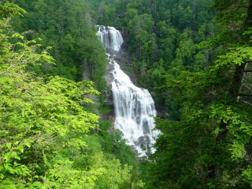 A stunning waterfall cascades down rocky cliffs, surrounded by lush green trees and vibrant foliage.