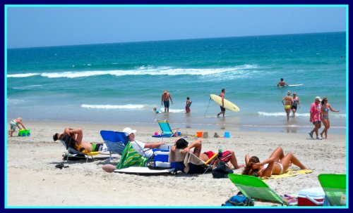 A sunny beach scene with people sunbathing, swimming, and surfing, surrounded by colorful beach chairs and umbrellas.