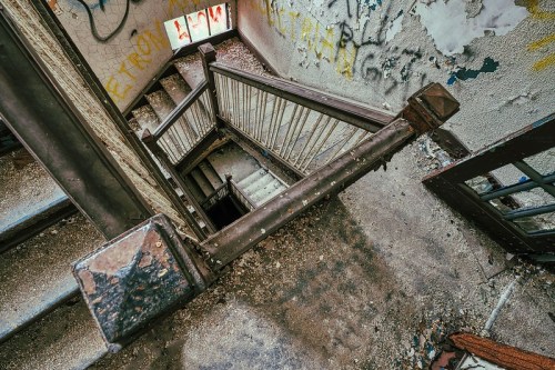 A view looking down an abandoned staircase with worn steps and graffiti on the walls.