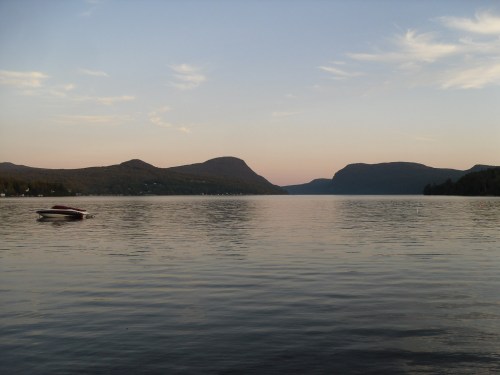 A serene lake at sunset, surrounded by mountains and a calm water surface reflecting the sky.