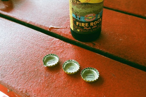 Three bottle caps on a red table, with a bottle of Fire Rock beer in the background.