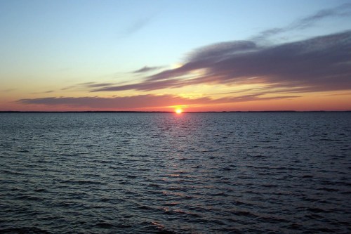 A serene sunset over calm waters, with vibrant colors reflecting on the surface and wispy clouds in the sky.