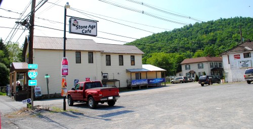A red pickup truck parked in front of the Stone Age Cafe, with a green hillside in the background and power lines overhead.