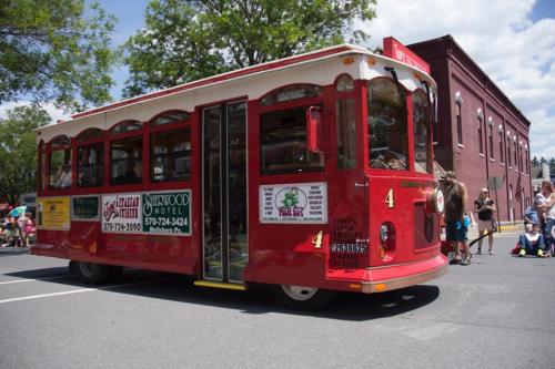 A red trolley car with large windows and advertisements, parked on a street during a sunny day.