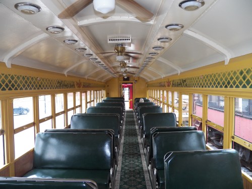 Interior of a vintage train car with green seats, yellow walls, and decorative ceiling lights.