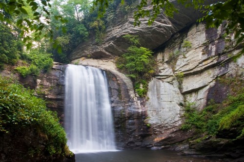 A serene waterfall cascading over rocky cliffs, surrounded by lush greenery and trees.