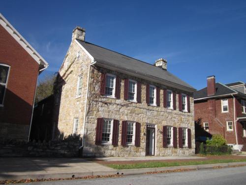 Historic stone house with red shutters, surrounded by trees and blue sky, showcasing classic architectural style.