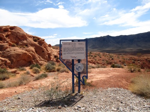 Sign for Arrowhead Trail in a desert landscape with rocky formations and sparse vegetation under a blue sky.