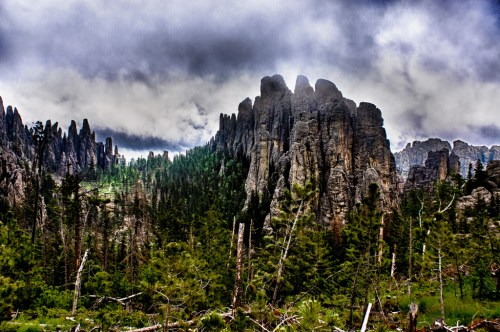 Dramatic mountain landscape with towering rock formations and dense forest under a cloudy sky.