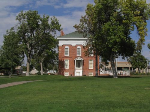 A red brick building with white trim, surrounded by green grass and trees, under a partly cloudy sky.