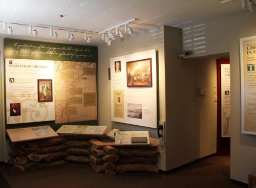 Exhibit space featuring historical displays, text panels, and artifacts, with logs arranged as a decorative element.