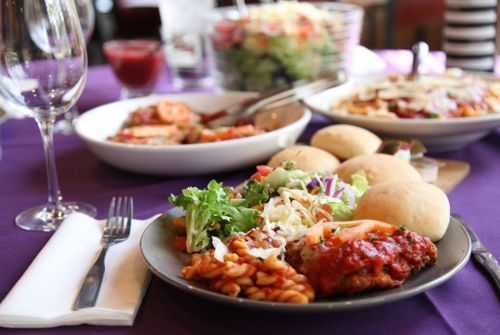A table set with a variety of dishes, including pasta, salad, rolls, and meat, on a purple tablecloth.