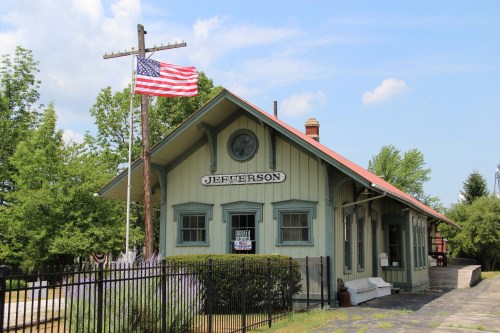 Historic train station with a sign reading "Jefferson," surrounded by trees and featuring an American flag.