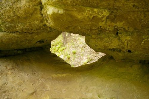 View through a natural rock formation, showcasing a hole with greenery visible beyond.