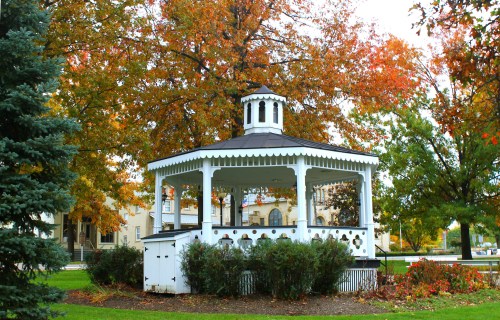 A white gazebo surrounded by colorful autumn trees in a park setting.