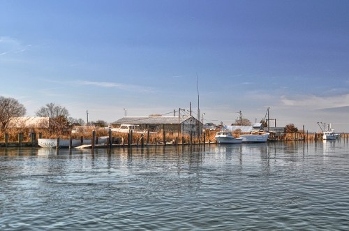 A calm waterway with boats and a rustic building along the shore under a clear blue sky.