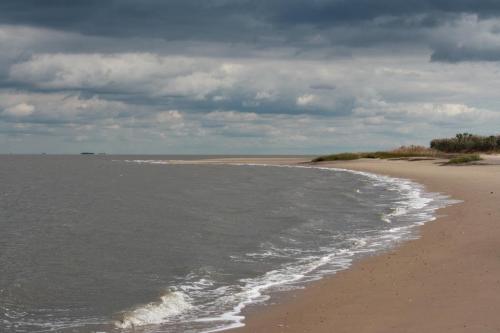 A calm beach scene with gentle waves, sandy shore, and overcast skies in the background.