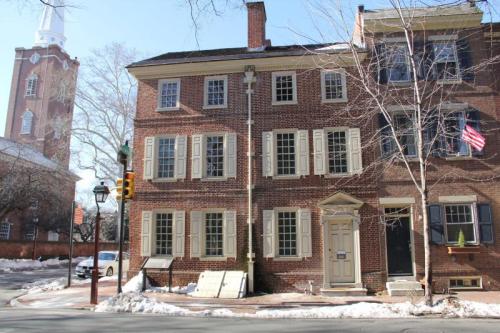 Historic brick building with green shutters, an American flag, and a church steeple in the background on a snowy street.