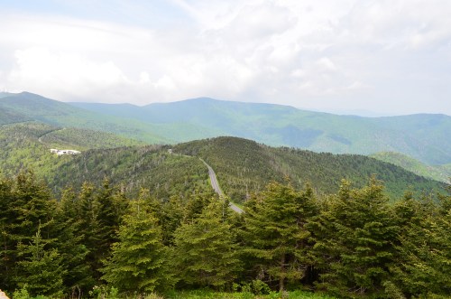 A scenic view of rolling green mountains and a winding road, with a cloudy sky above.
