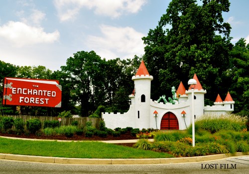 A whimsical castle with red-tipped towers, surrounded by greenery, next to a vintage sign reading "The Enchanted Forest."