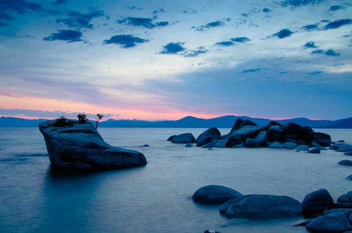 A serene landscape featuring rocky formations by a calm lake at dusk, with soft clouds and a colorful sky.