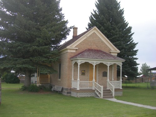 A historic brick house with a porch, surrounded by trees and a grassy area.