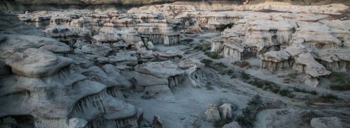 A rugged landscape of eroded rock formations and sandy terrain under soft lighting.