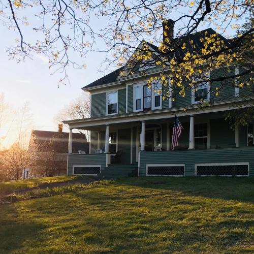 A charming green house with a porch, American flag, and blooming trees, bathed in warm sunset light.