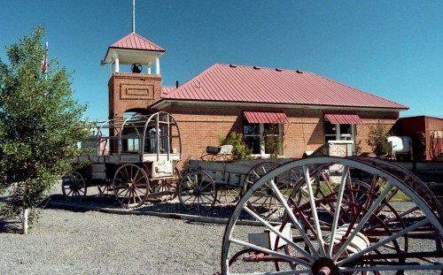 Historic building with a red roof, surrounded by vintage wagons and greenery under a clear blue sky.