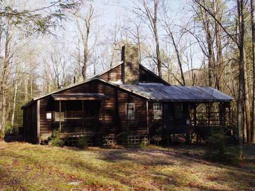 A rustic wooden cabin surrounded by trees, featuring a stone chimney and a porch.