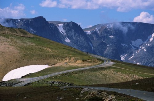 A winding road through a mountainous landscape with snow patches and blue skies.