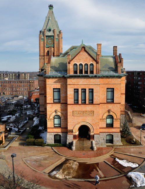 Historic brick building with a clock tower, surrounded by a paved area and snow, under a clear sky.