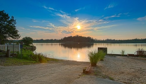 A serene lake at sunset, with vibrant clouds reflecting on the water and lush greenery along the shore.