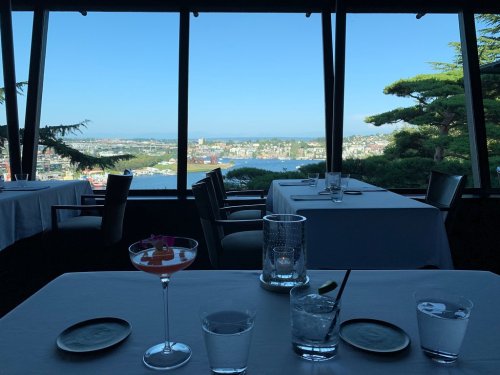 A restaurant table with drinks, overlooking a scenic view of a harbor and cityscape through large windows.