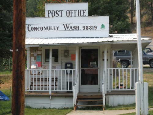 A small, rustic post office building with a sign reading "Post Office" and "Conconully Wash. 98819."