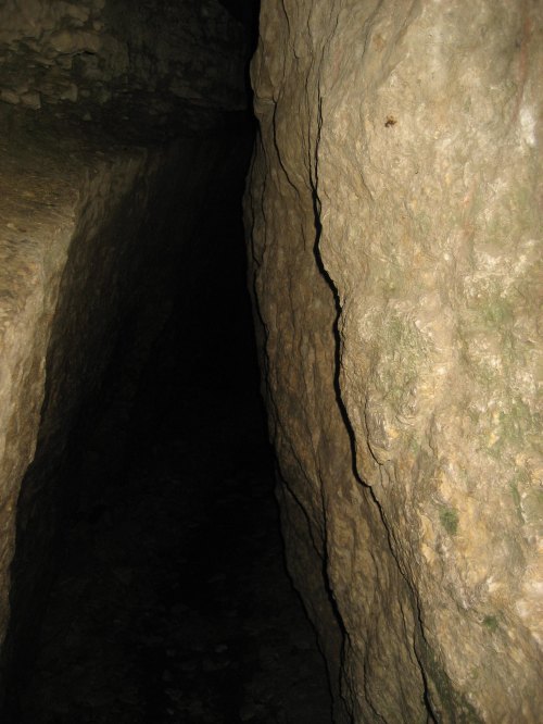 A narrow, dark crevice between two rocky walls, with rough textures and shadows.