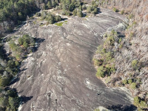 Aerial view of a rocky landscape with patches of greenery and sparse trees on a sloped surface.