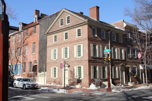 Historic brick buildings on a snowy street corner, featuring traditional architecture and green shutters.