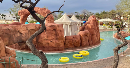 A winding pool surrounded by rocky formations and trees, with yellow inner tubes floating on the water.