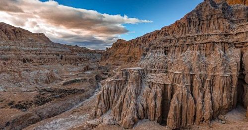 A rugged landscape featuring towering rock formations and a dramatic sky with clouds.