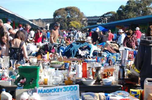 A bustling outdoor market filled with people browsing through various items and antiques on display.