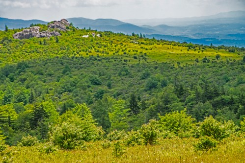 Lush green hills and rocky outcrops under a cloudy sky, with distant mountains in the background.