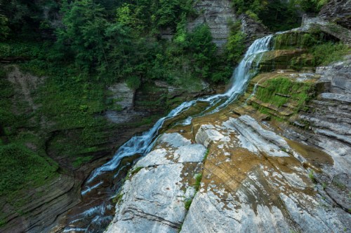 A serene waterfall cascades over rocky cliffs, surrounded by lush greenery and flowing water.