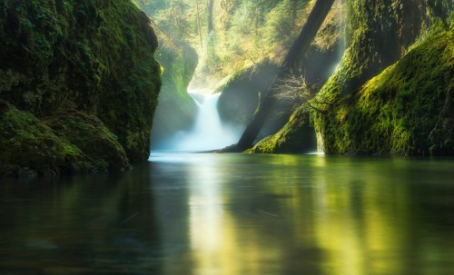 A serene landscape featuring a tranquil river flowing through lush, moss-covered rocks and a gentle waterfall in the background.