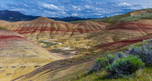 Colorful, layered hills of the Painted Hills in Oregon, showcasing vibrant reds, yellows, and greens under a cloudy sky.