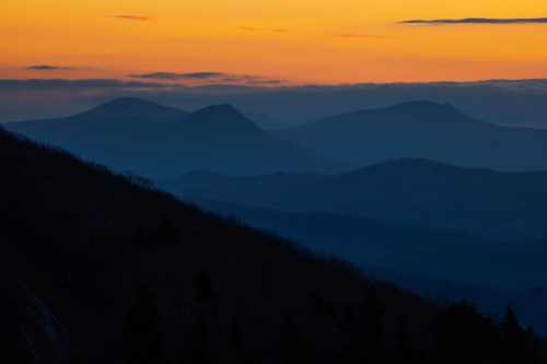 Silhouetted mountains against a vibrant orange and blue sunset sky, with layers of misty hills in the foreground.