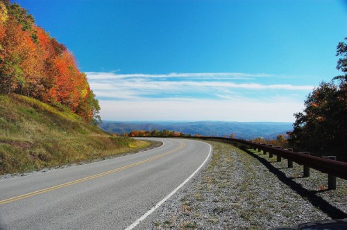 A winding road curves through a landscape of vibrant autumn foliage under a clear blue sky.