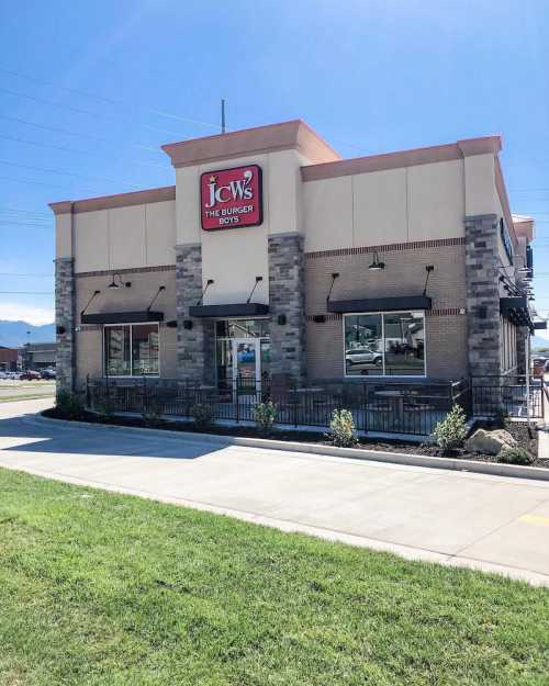 A modern fast-food restaurant with a sign reading "JCW's The Burger Boys," featuring a stone and stucco exterior.