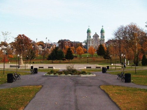 A park pathway leads to a distant building with green domes, surrounded by autumn trees and benches.